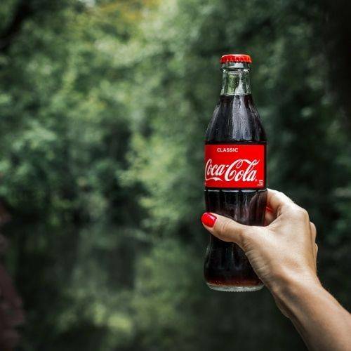 woman with painted nails holds bottle of coke